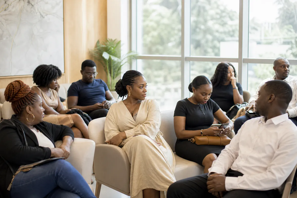 Kenyan men and women with various skin tones and ages sit together in a bright clinic waiting room, showing different skin concerns.