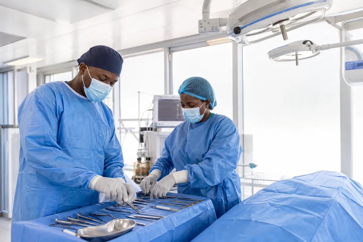Two surgeons in blue scrubs and masks prepare surgical instruments in a bright, high-tech operating room.