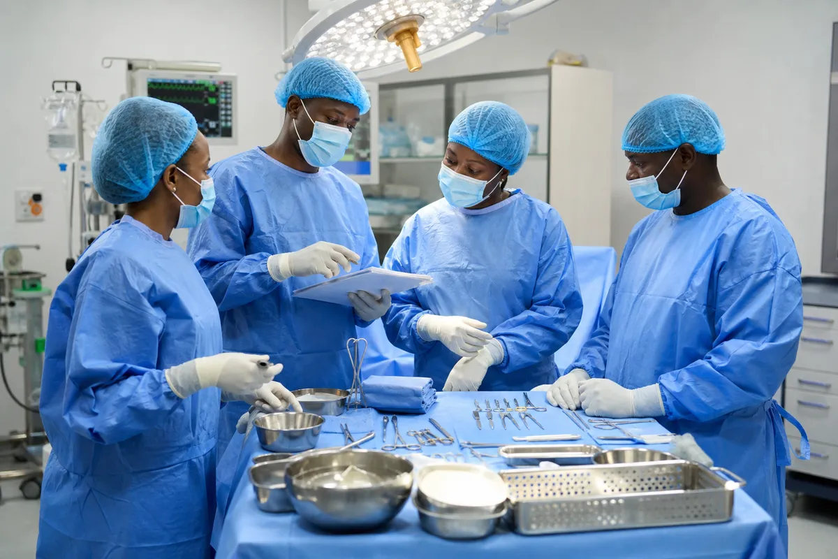 A group of African medical professionals in surgical attire checks instruments and coordinates before a breast surgery in a bright, sterile operating theatre.